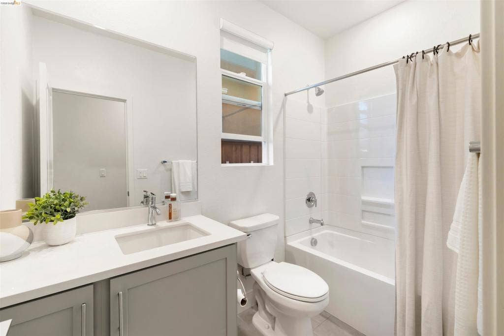 539 Gemstone Way, Oakley, CA 94561 Grey cabinetry, white solid-surface countertop with an integrated rectangular sink, large wall-mounted mirror, vertical window, and a bathtub with a tiled surround