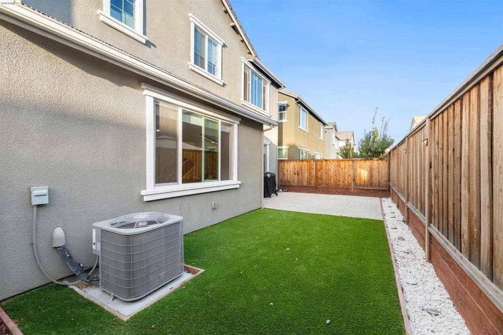 539 Gemstone Way, Oakley, CA 94561 Exterior side yard featuring synthetic turf, concrete patio, wood-style privacy fencing, and a gravel border