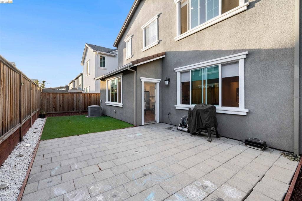539 Gemstone Way, Oakley, CA 94561 Rear exterior featuring a paver patio, synthetic turf lawn, wood-panel fencing, and a side-mounted light fixture