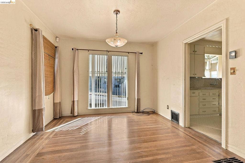 2901 Sheffield Ave, Oakland, CA 94602 Interior room featuring wood-finish flooring, a central decorative pendant light fixture, and large windows with vertical blinds