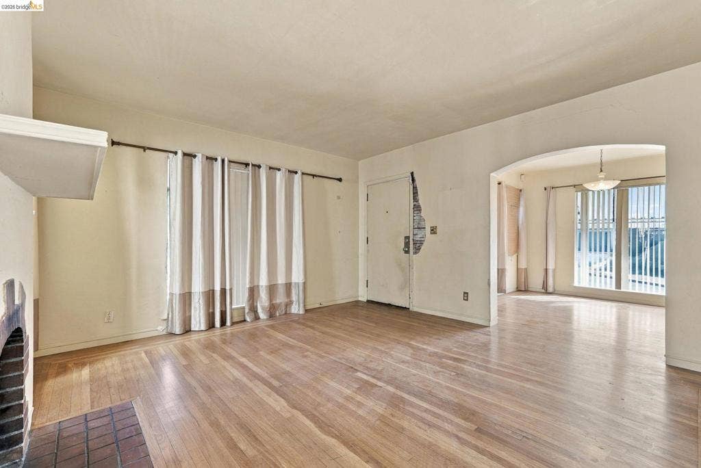 2901 Sheffield Ave, Oakland, CA 94602 Open floor plan featuring wood-finish flooring, a masonry fireplace with a brick hearth, and an arched entryway