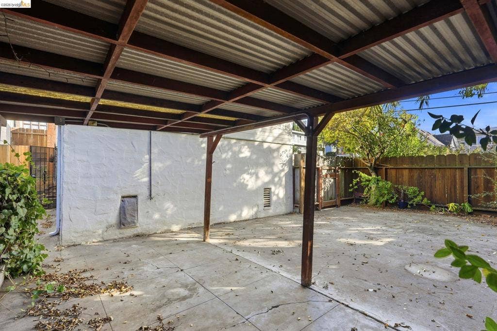2901 Sheffield Ave, Oakland, CA 94602 Covered carport featuring a metal roof, exposed timber beam support structure, concrete flooring, and wood perimeter fencing
