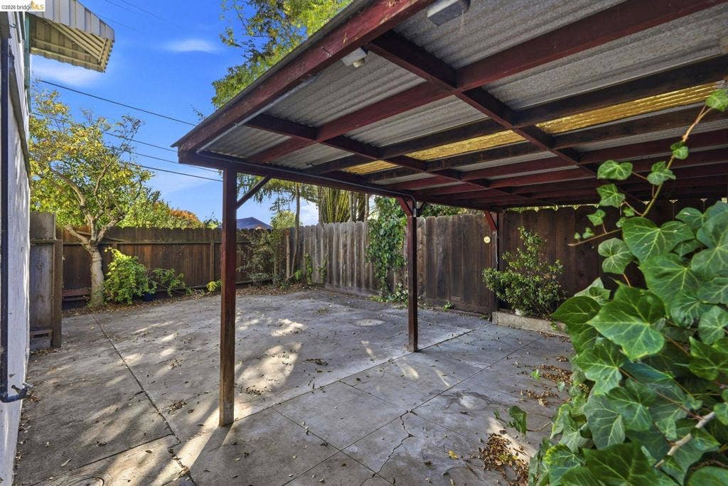 2901 Sheffield Ave, Oakland, CA 94602 Covered carport featuring a metal roof, exposed timber beams, and a concrete slab foundation, enclosed by vertical wood fencing