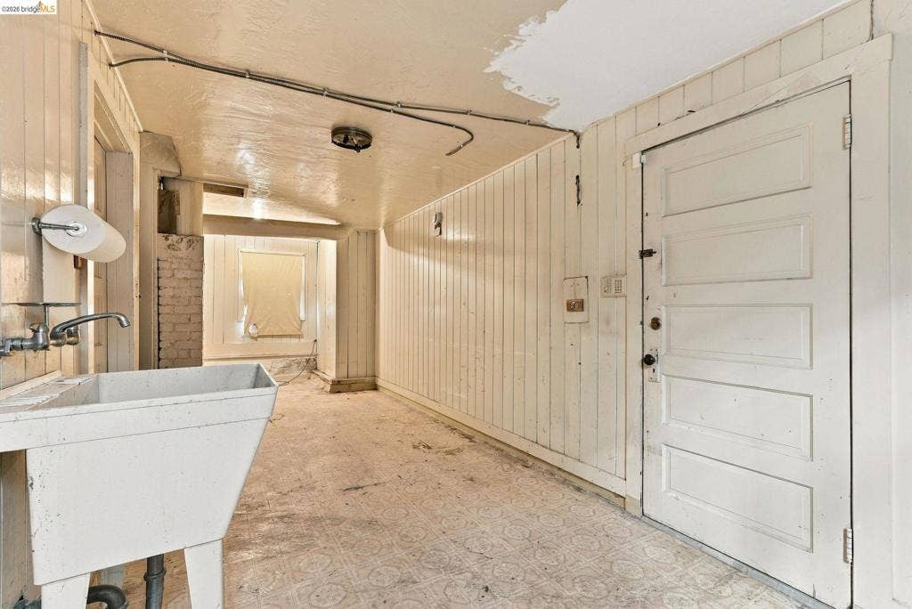 2901 Sheffield Ave, Oakland, CA 94602 Utility area featuring vertical paneled wall cladding, patterned resilient flooring, a free-standing basin sink, and a five-panel wood door