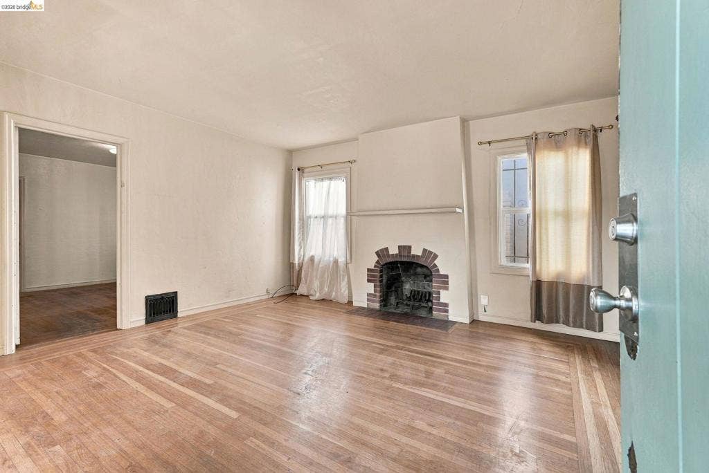 2901 Sheffield Ave, Oakland, CA 94602 Living area featuring wood-finish flooring, a masonry fireplace with an arched hearth, and multipane windows