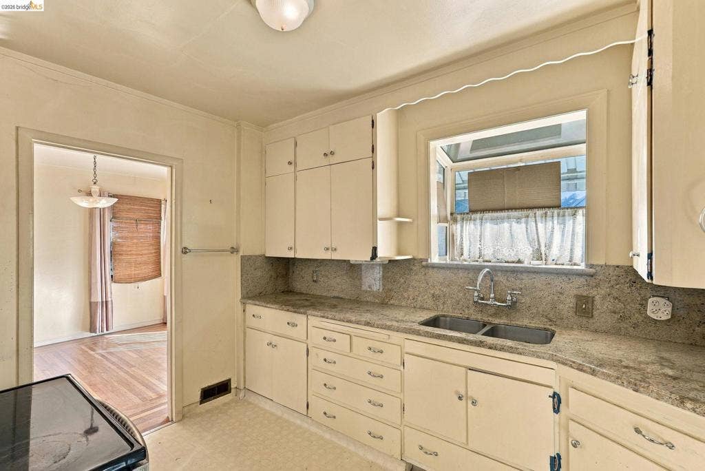 2901 Sheffield Ave, Oakland, CA 94602 Kitchen featuring stone-finish countertops, dual-basin stainless steel sink with a goose-neck faucet, painted cabinetry with integrated hardware, and a garden window