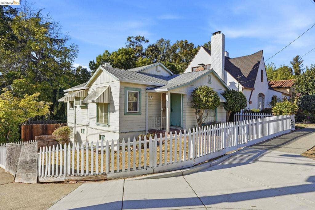 2901 Sheffield Ave, Oakland, CA 94602 Single-story residence featuring horizontal siding, a pitched roofline, metal window awnings, and a white picket fence enclosing the front yard