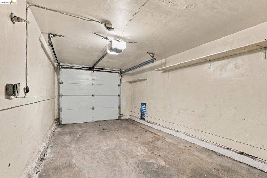 2901 Sheffield Ave, Oakland, CA 94602 Garage interior featuring a sectional overhead door, automatic door opener, and wall-mounted shelving