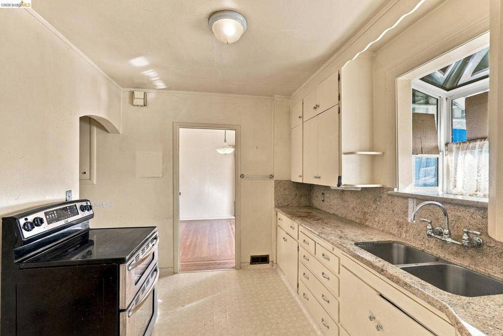 2901 Sheffield Ave, Oakland, CA 94602 Kitchen featuring painted cabinetry, stone-surface countertops, dual-basin stainless steel sink, and black electric range