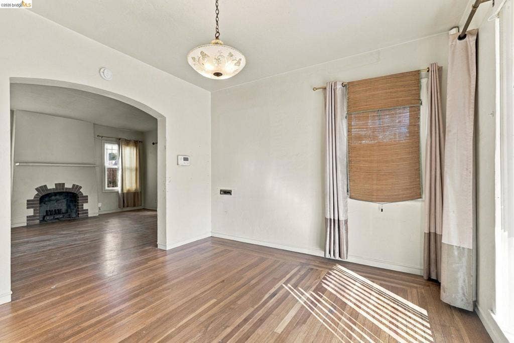2901 Sheffield Ave, Oakland, CA 94602 Hardwood flooring, arched doorway, and masonry fireplace surround, illuminated by a vintage-style flush-mount pendant fixture