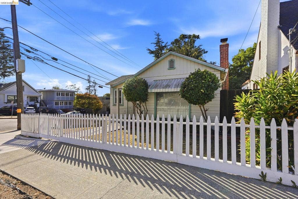 2901 Sheffield Ave, Oakland, CA 94602 Exterior facade featuring wood-style horizontal siding, a classic gabled roofline, a decorative metal window awning, an exposed brick chimney, and a white picket fence