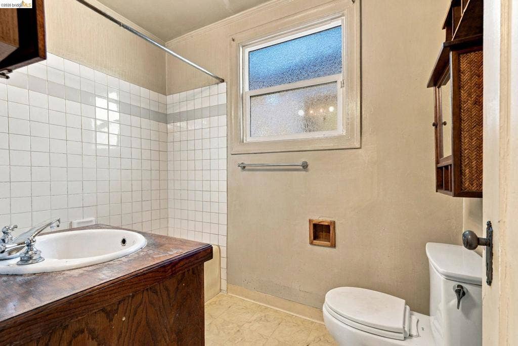 2901 Sheffield Ave, Oakland, CA 94602 Bathroom featuring a wood vanity with a drop-in sink, white tile shower surround, obscured glass window, and built-in wall recessed shelving
