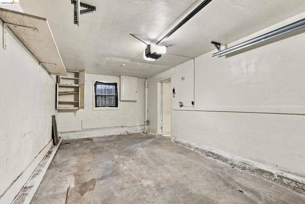 2901 Sheffield Ave, Oakland, CA 94602 Garage space featuring concrete flooring, built-in wall shelving, painted masonry walls, and an overhead automatic door opener system