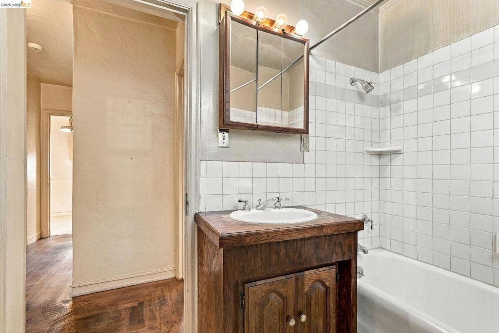 2901 Sheffield Ave, Oakland, CA 94602 Bathroom featuring a wood-finish vanity with a drop-in sink, tripartite medicine cabinet with integrated lighting, and a white tiled shower surround