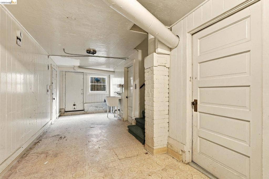 2901 Sheffield Ave, Oakland, CA 94602 Painted brick pillar, beadboard wall paneling, utilitarian utility basin, multi-panel wood doors, and patterned vinyl flooring
