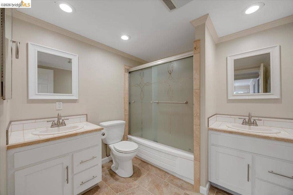 5827 Lookout Ct, CA 95233 Dual white vanities featuring light-toned countertops and undermount sinks, bathtub with a decorative etched glass sliding enclosure, recessed lighting, and tile flooring