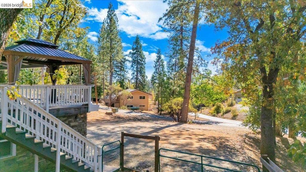 5827 Lookout Ct, CA 95233 Elevated deck featuring a covered gazebo, stone-faced foundation, and wood-railing enclosure, set among mature trees