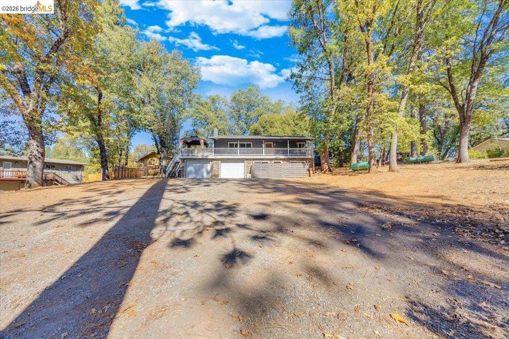 5827 Lookout Ct, CA 95233 Exterior featuring a two-car garage, elevated deck with white railing, and extensive surrounding mature trees