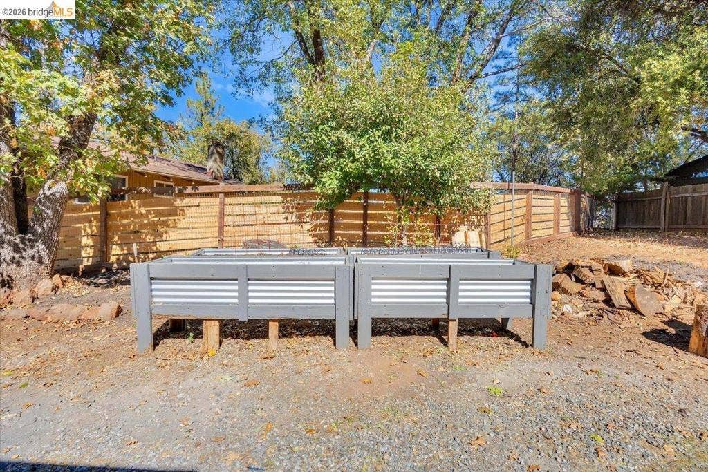 5827 Lookout Ct, CA 95233 Raised garden beds featuring gray-painted frames and corrugated metal siding, enclosed by a horizontal wood-slat privacy fence