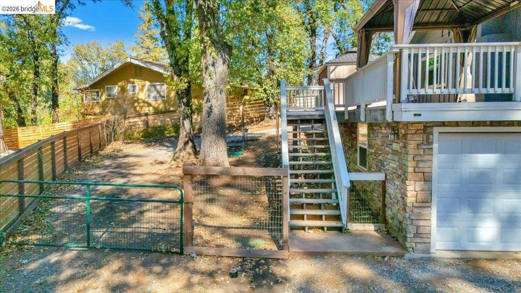 5827 Lookout Ct, CA 95233 Exterior featuring a stone-clad lower level, elevated wooden deck with white railing, built-in staircase, and fenced perimeter