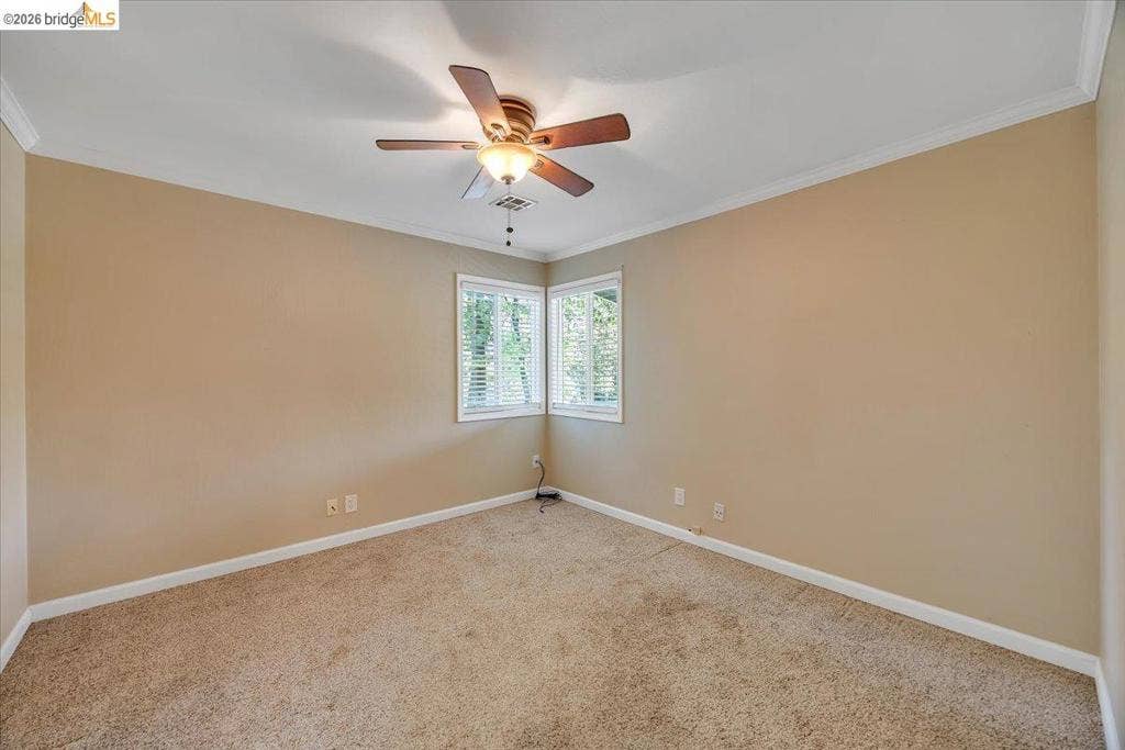 5827 Lookout Ct, CA 95233 Neutral wall tones, carpeting, crown molding, corner windows with blinds, and a ceiling-mounted light fixture with a fan