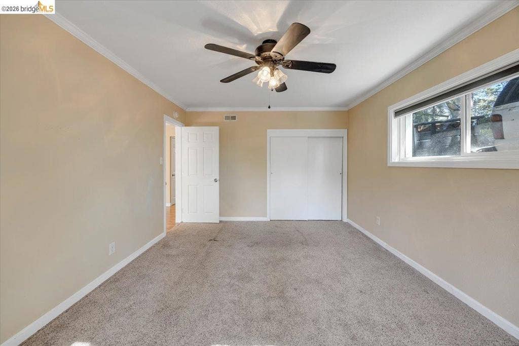 5827 Lookout Ct, CA 95233 Neutral-toned interior featuring wall-to-wall carpeting, a multi-blade ceiling fan with integrated lighting, sliding-panel closet doors, and a horizontal window