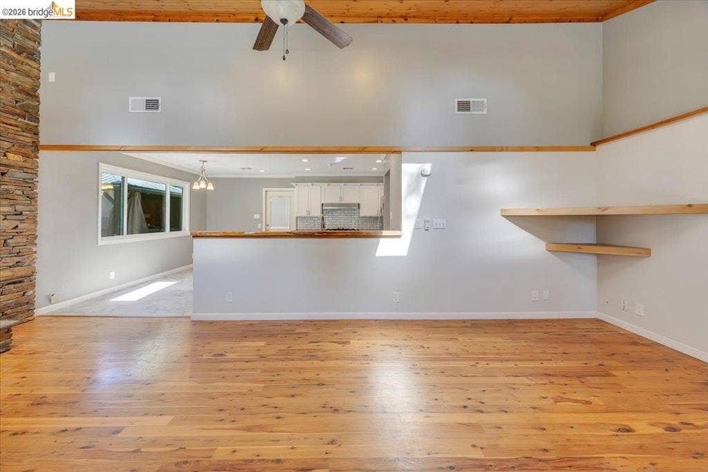 5827 Lookout Ct, CA 95233 High ceilings with exposed wood-beam detailing, floor-to-ceiling stone accent wall, wood-finish flooring, and built-in floating shelves