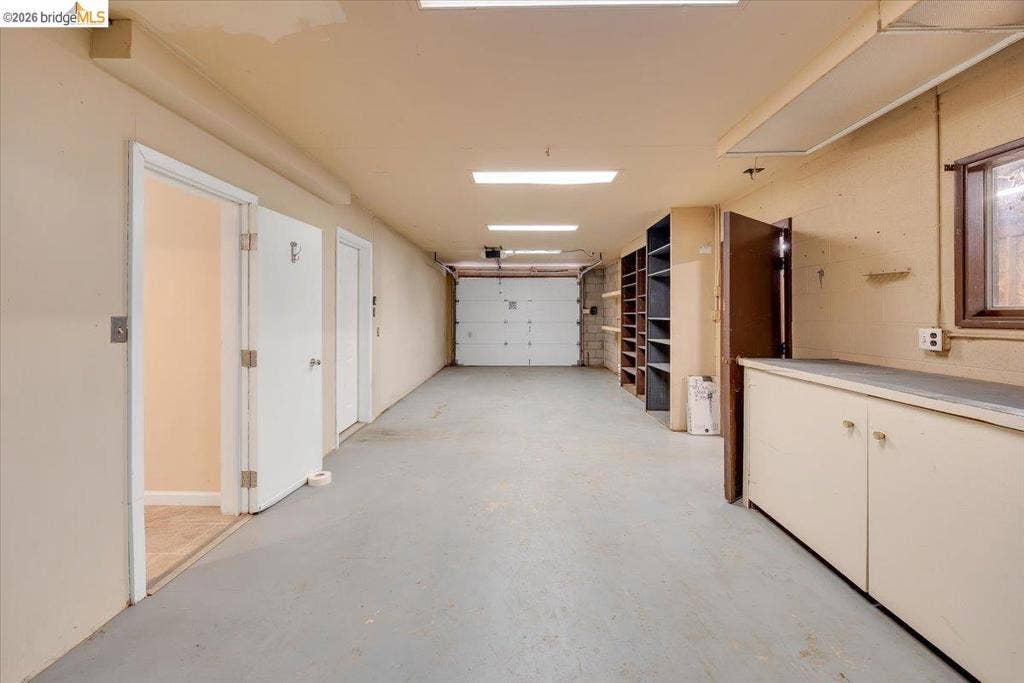 5827 Lookout Ct, CA 95233 Multi-vehicle garage featuring a sectional overhead door, built-in floor-to-ceiling shelving, solid-surface cabinetry, and fluorescent lighting