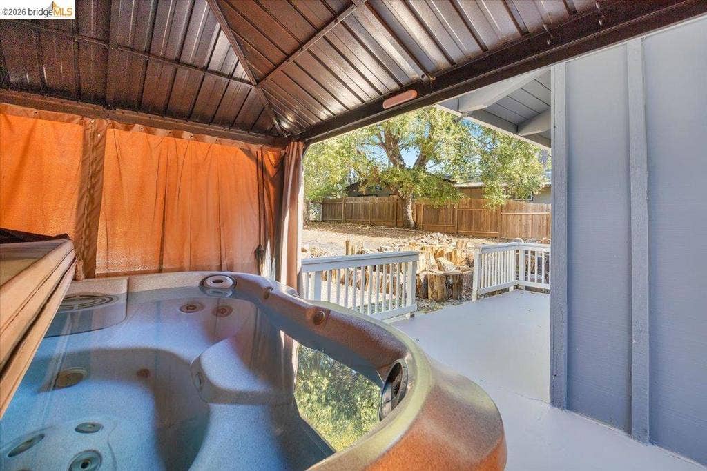 5827 Lookout Ct, CA 95233 Covered spa area featuring a built-in hot tub, metal roof structure, wood-style decking, and white balustrade railing