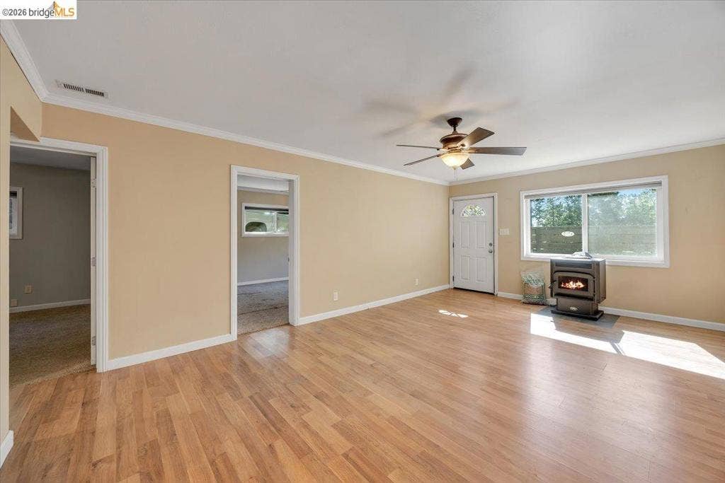5827 Lookout Ct, CA 95233 Living area featuring wood-finish flooring, a ceiling fan, crown molding, a wood-burning stove, and a white entry door with glass paneling