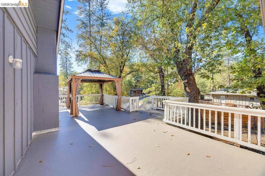 5827 Lookout Ct, CA 95233 Spacious deck featuring vertical board siding, white baluster railings, a built-in gazebo structure with a metal roof, and wall-mounted exterior lighting