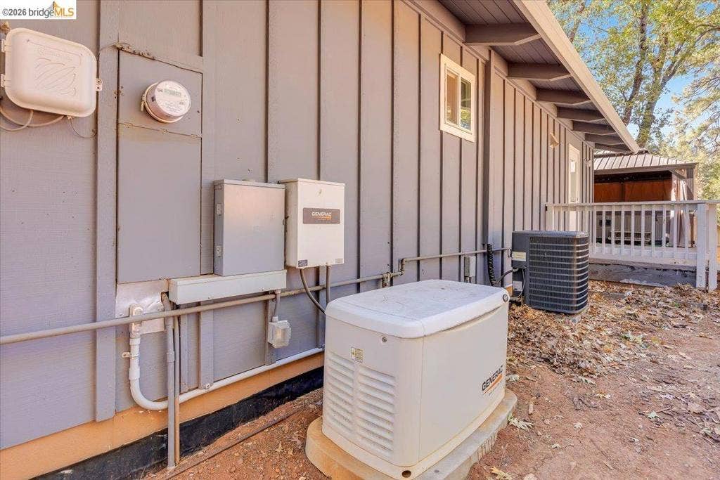 5827 Lookout Ct, CA 95233 Exterior wall featuring vertical board-and-batten siding, a dedicated whole-home standby generator, an HVAC condenser unit, and a railed outdoor deck structure