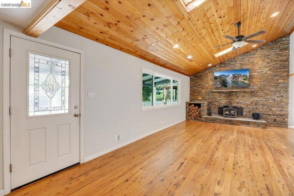 5827 Lookout Ct, CA 95233 Vaulted wood-plank ceiling featuring recessed lighting and a ceiling fan, stacked-stone accent wall with integrated hearth, wood-finish flooring, and exterior door with decorative glass inlay