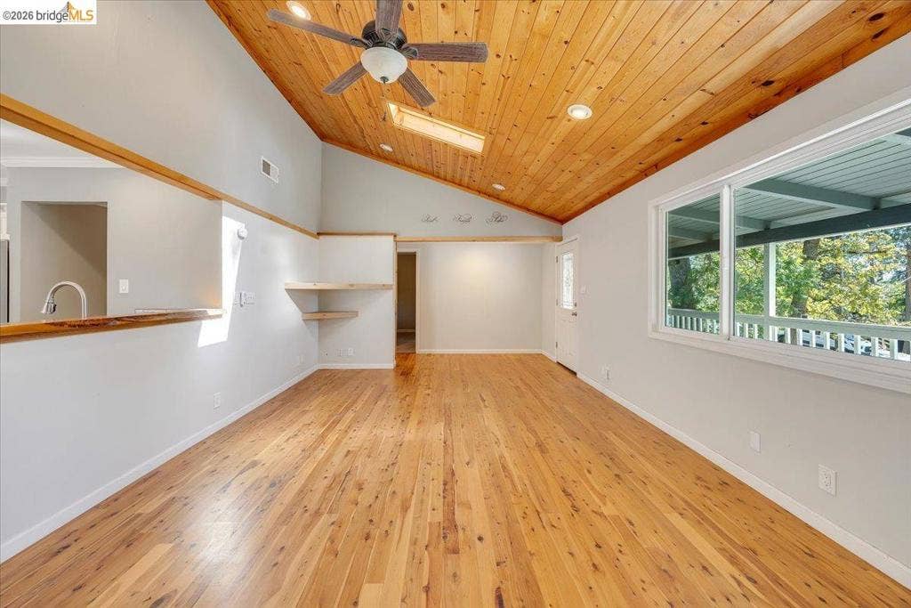 5827 Lookout Ct, CA 95233 Vaulted wood-plank ceiling featuring a skylight and integrated ceiling fan, wood-finish flooring, built-in shelving, and large windows