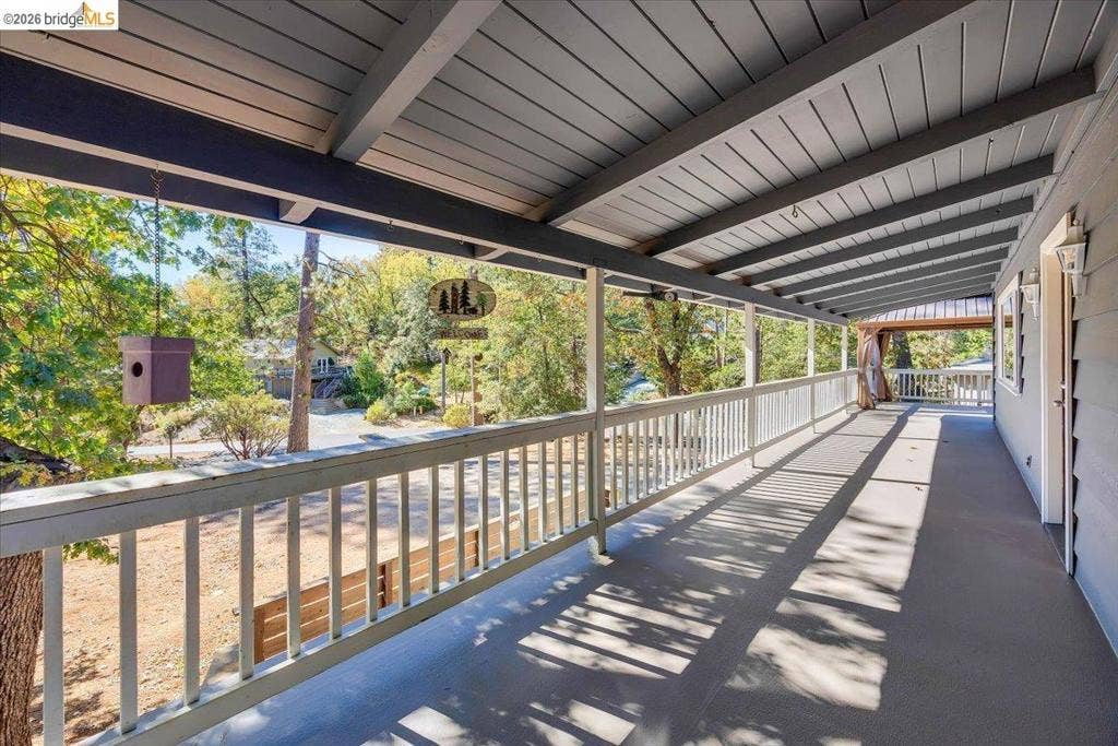 5827 Lookout Ct, CA 95233 Covered deck featuring wood-paneled ceiling, exposed beam supports, painted wood railing, and wall-mounted exterior lighting