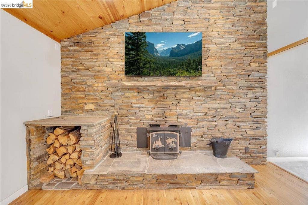 5827 Lookout Ct, CA 95233 Full-height dry-stacked stone fireplace wall featuring a wood-burning stove, integrated stone hearth, built-in firewood storage compartment, and natural wood-plank ceiling