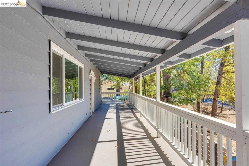 5827 Lookout Ct, CA 95233 Covered exterior deck featuring exposed beam ceiling, white picket railing, and smooth surface flooring
