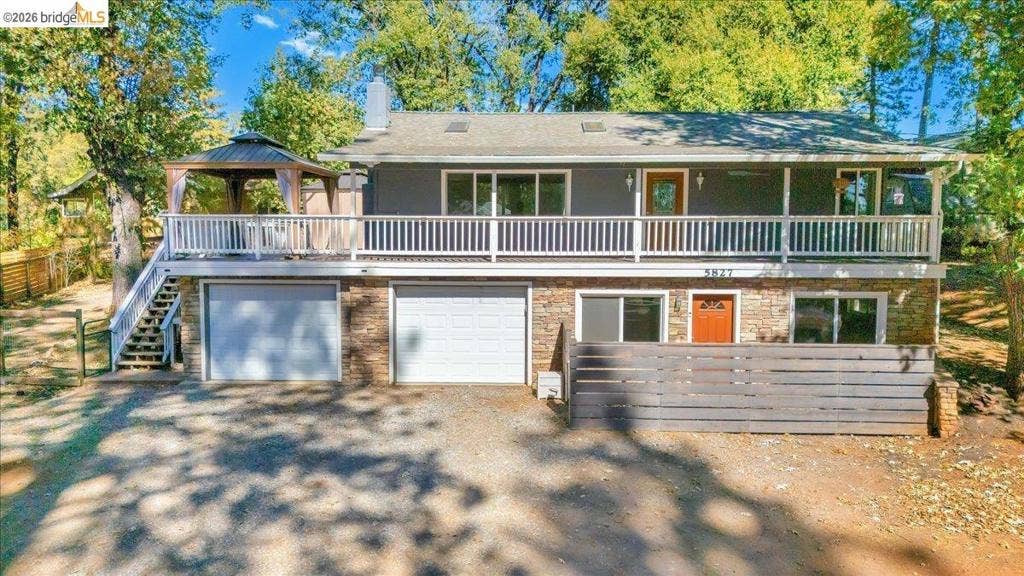 5827 Lookout Ct, CA 95233 Split-level exterior featuring stone veneer siding, an expansive upper-level deck with white railing, a double-bay garage, and a wood-slat privacy screen