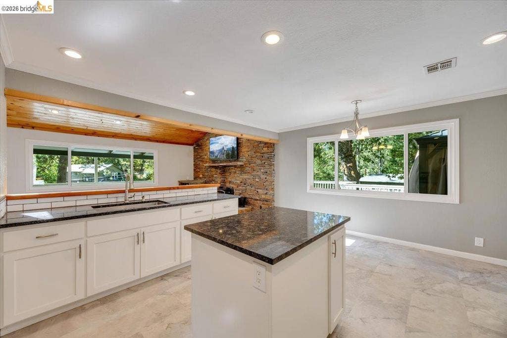 5827 Lookout Ct, CA 95233 Kitchen featuring stone-finish countertops, white shaker-style cabinetry, a stone-clad accent wall, tile flooring, and a wood-plank ceiling soffit