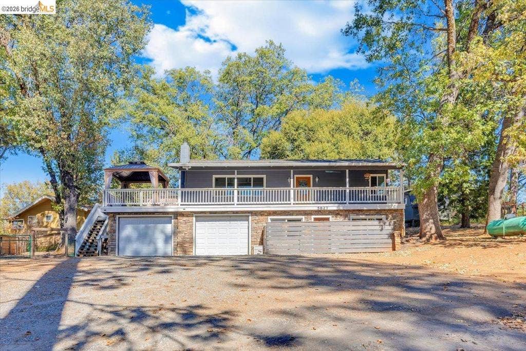 5827 Lookout Ct, CA 95233 Exterior featuring a two-story elevation, horizontal siding, stone veneer lower level, wide upper-level railed deck, and dual garage bays