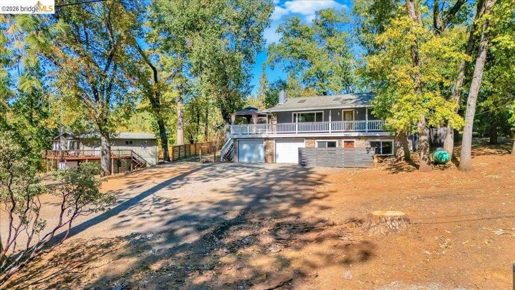 5827 Lookout Ct, CA 95233 Two-story residence featuring a wood-sided exterior, wrap-around deck with white railing, double-car garage, and mature trees on a spacious lot