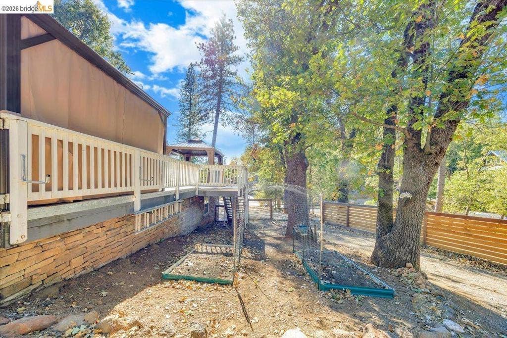 5827 Lookout Ct, CA 95233 Raised deck with white railing, natural stone foundation, wood-slat perimeter fencing, and raised garden beds
