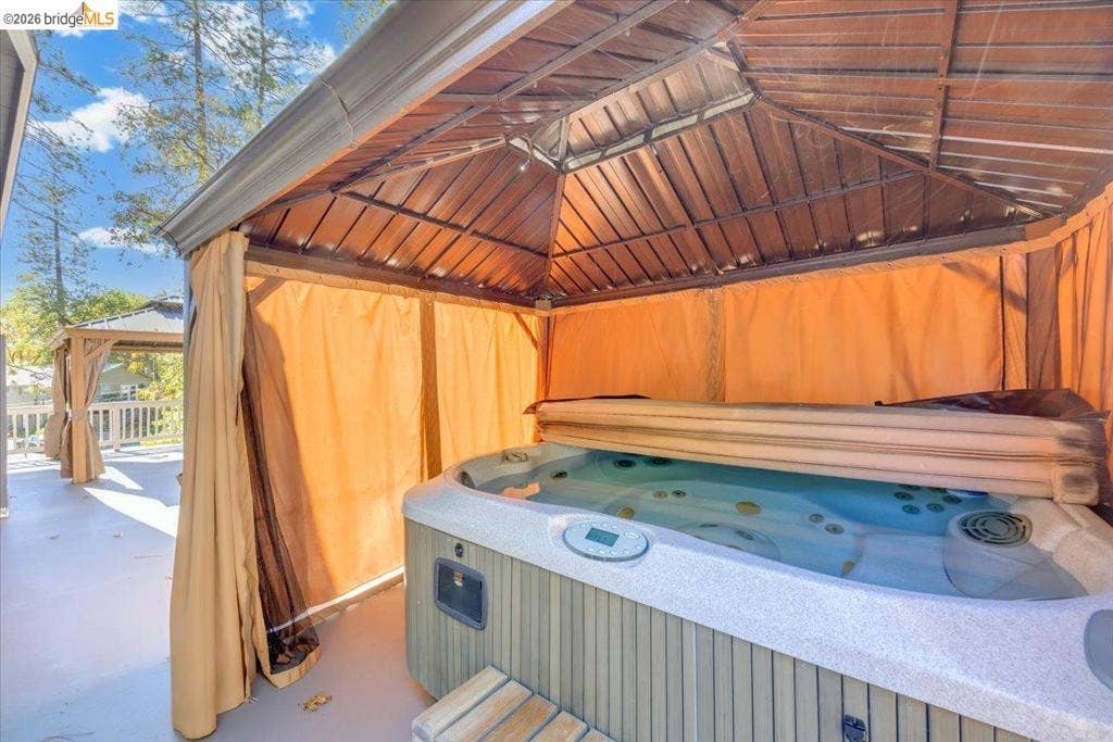 5827 Lookout Ct, CA 95233 Outdoor spa with a molded basin, integrated jetting system, and exterior side paneling, sheltered by a peaked roof gazebo featuring a slatted ceiling structure
