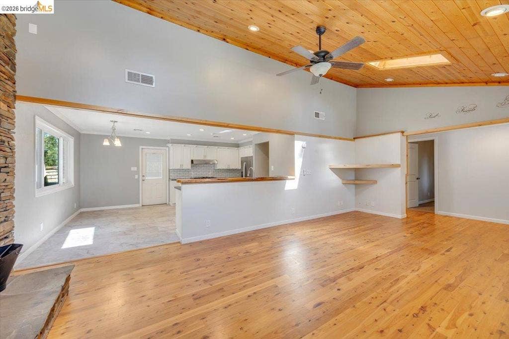 5827 Lookout Ct, CA 95233 Vaulted wood-plank ceiling featuring a skylight and ceiling fan, wood-finish flooring, stone fireplace surround, and a breakfast bar with a wood countertop
