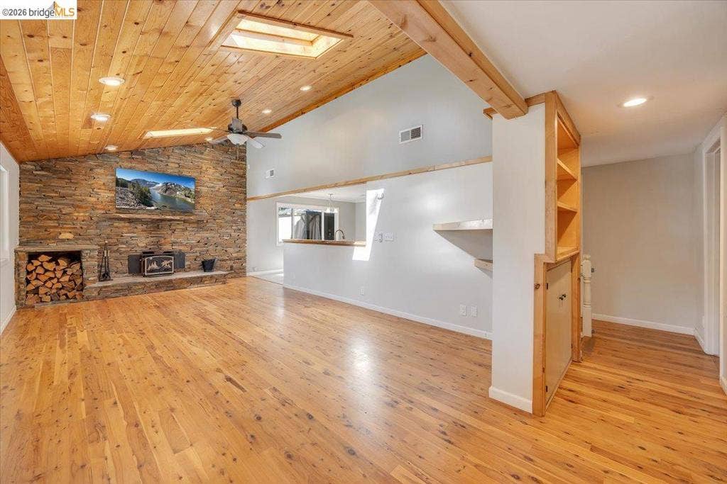 5827 Lookout Ct, CA 95233 Vaulted ceiling with wood-plank finish and skylight, floor-to-ceiling stone accent wall, integrated masonry wood-burning hearth, wood-finish flooring, and built-in wooden shelving