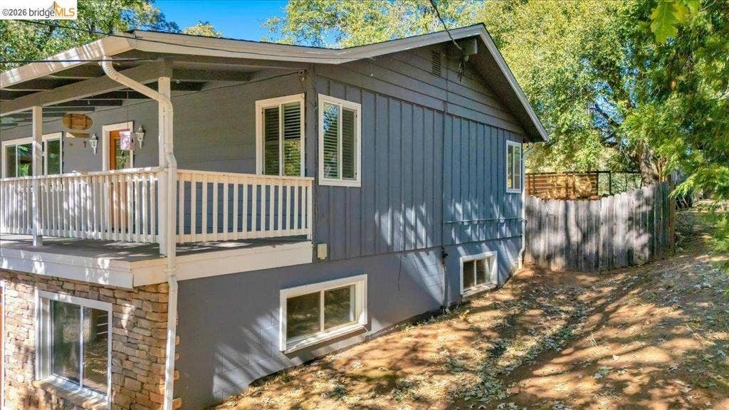 5827 Lookout Ct, CA 95233 Exterior featuring vertical board-and-batten siding, a stone veneer foundation, a raised deck with white railing, and a fenced exterior area