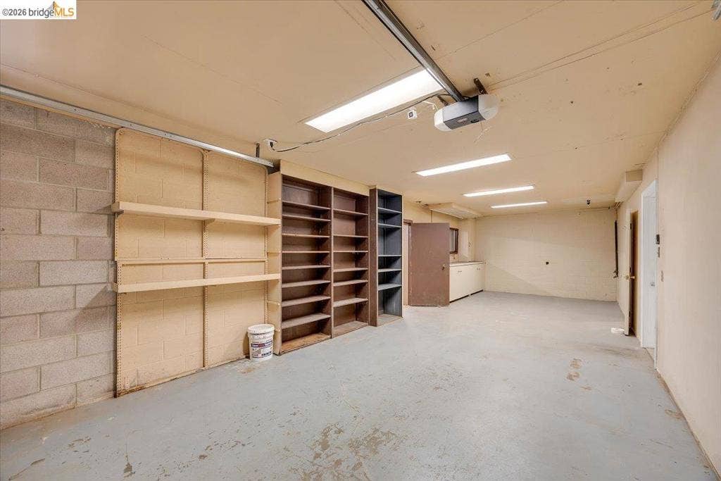 5827 Lookout Ct, CA 95233 Interior space featuring concrete block walls, integrated wood-finish shelving units, recessed linear lighting, and painted concrete flooring
