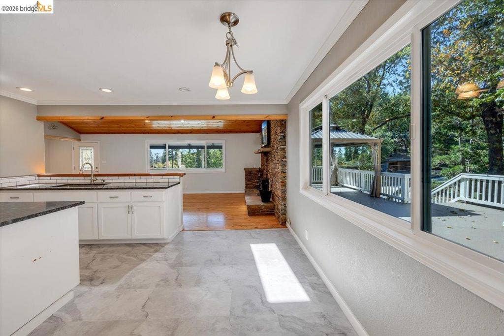 5827 Lookout Ct, CA 95233 Kitchen featuring white cabinetry, dark countertops, tile flooring, large multi-pane windows, and a stone-accented fireplace