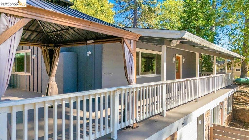 5827 Lookout Ct, CA 95233 Elevated deck featuring a white balustrade, integrated metal-framed gazebo, and neutral-toned surfacing