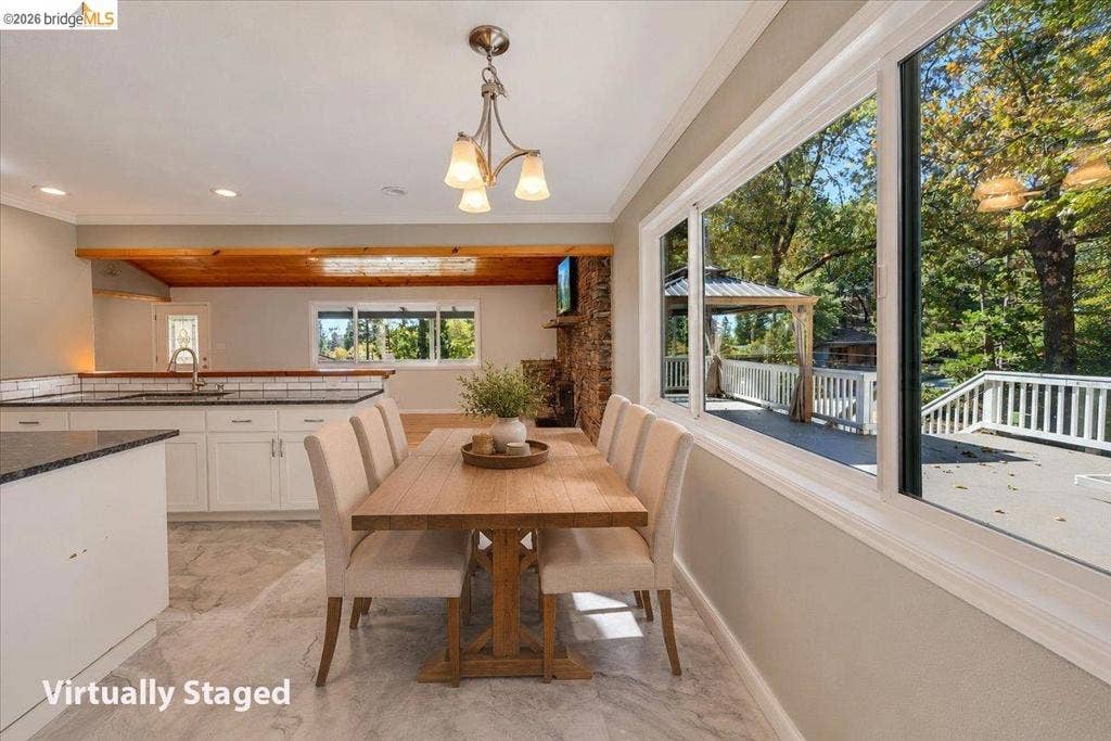 5827 Lookout Ct, CA 95233 Dining area featuring stone-finish flooring, expansive windows, built-in white cabinetry with dark countertops, a vaulted wood-beam ceiling, and a prominent stone fireplace surround